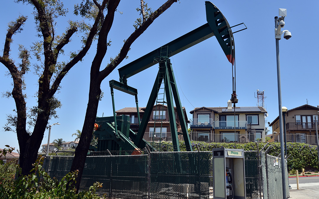 Fenced-in oil pump with houses in the background with