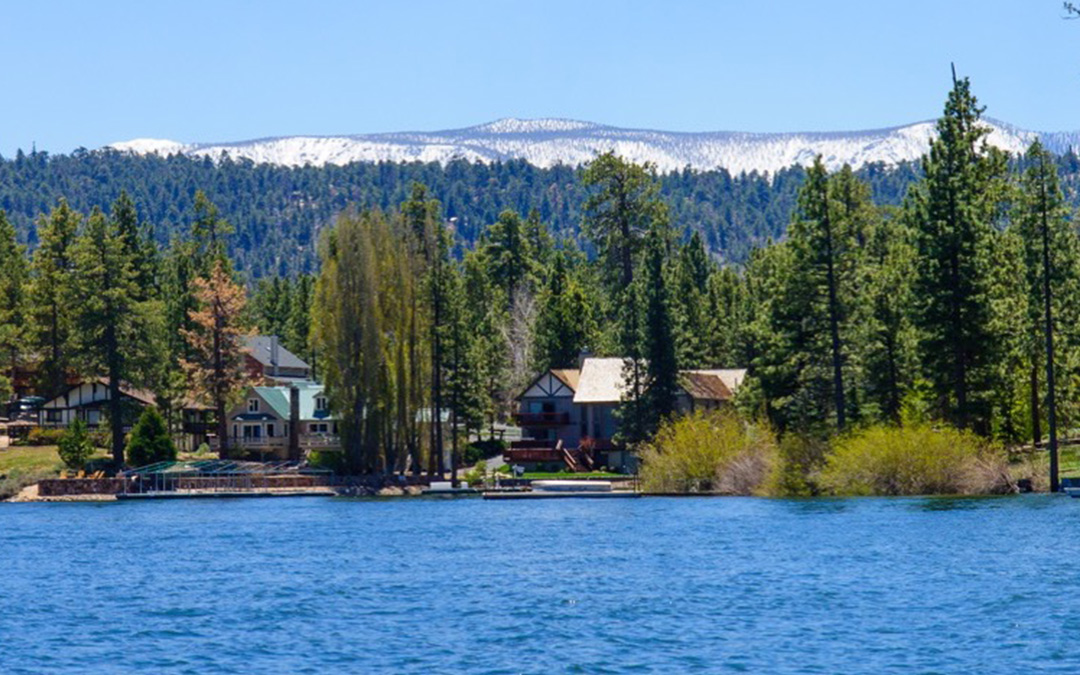lake with trees, houses and mountains in the background